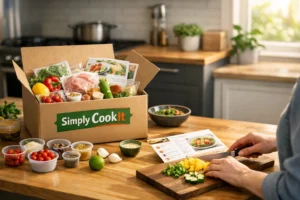 Hands preparing meal beside Simply CookIt box with fresh ingredients on a wooden counter in a kitchen.